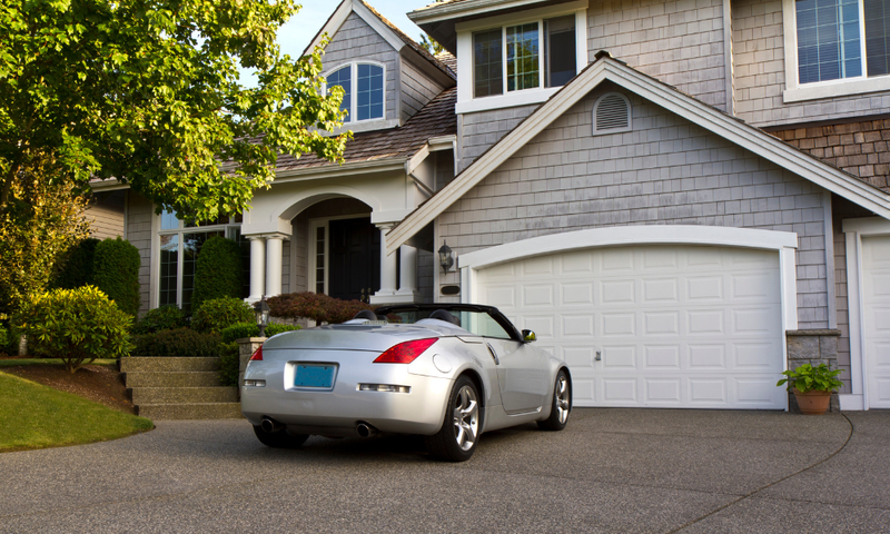 Silver convertible car parked in front of a house with a white garage door.
